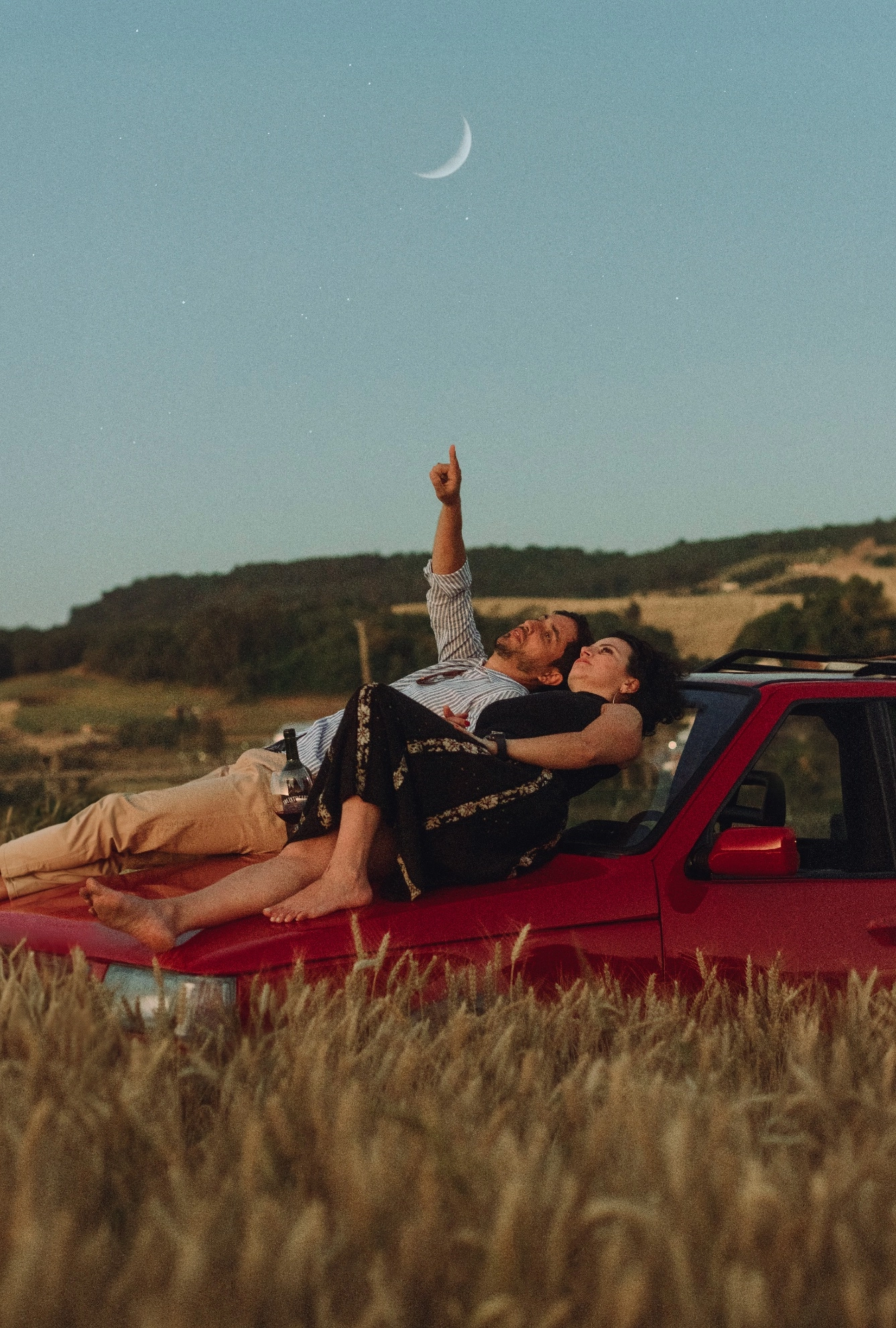 Casal em um carro vermelho ao entardecer